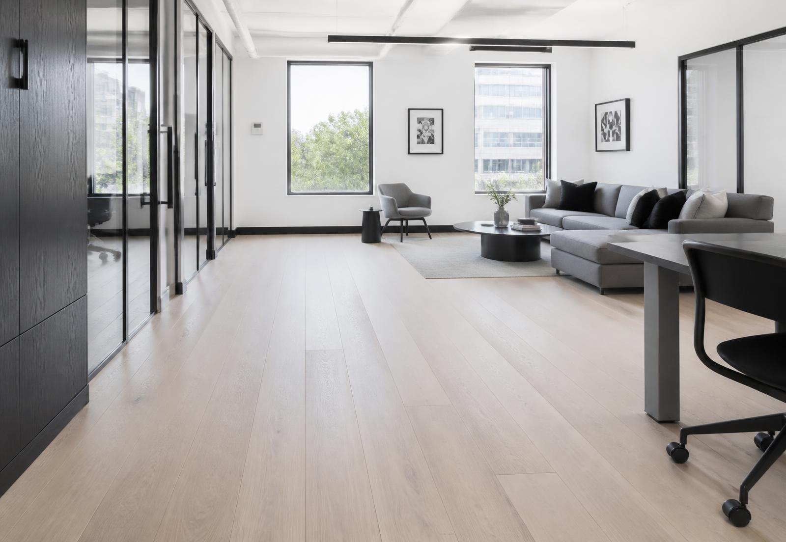 Open workplace interior with a light wood floor running toward tall windows